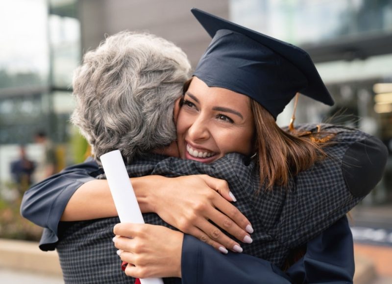 Portrait of a happy student hugging her father and celebrating her graduation - education concepts
